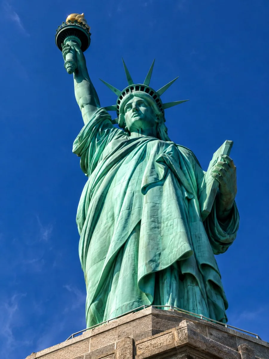 Mirando hacia arriba a la Estatua de la Libertad desde el balcón del pedestal, los pliegues verdes de cobre del vestido llenan el encuadre contra el cielo