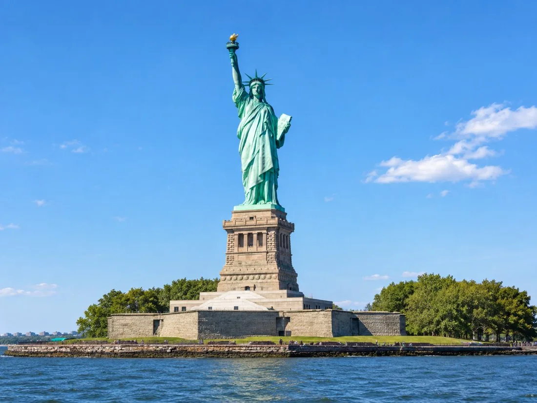 La Estatua de la Libertad, de cobre verde sobre un cielo azul despejado, vista desde el agua con la antorcha en alto
